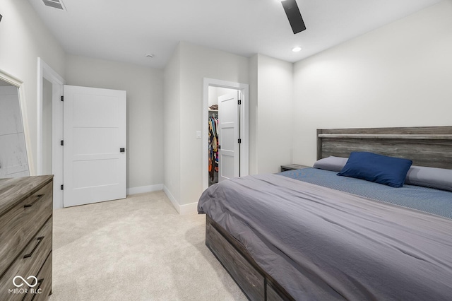 bedroom with light carpet, a walk in closet, a ceiling fan, baseboards, and a closet