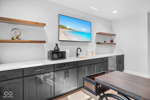 bar with black microwave, beverage cooler, light wood-style flooring, a sink, and wet bar