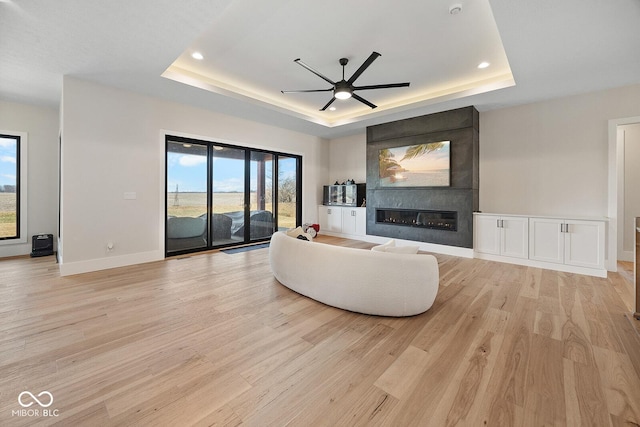 living room with a ceiling fan, a raised ceiling, a wealth of natural light, and a fireplace