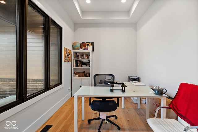home office featuring visible vents, a raised ceiling, baseboards, light wood finished floors, and recessed lighting