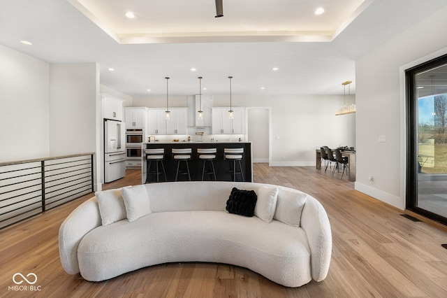 living area with light wood-type flooring, a tray ceiling, and recessed lighting