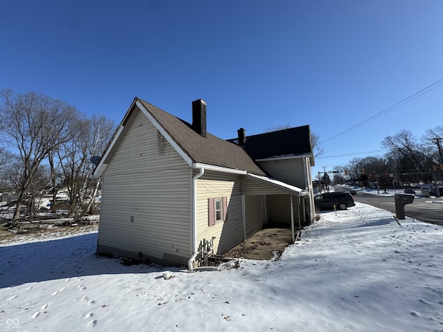 view of snow covered exterior featuring roof with shingles and a chimney