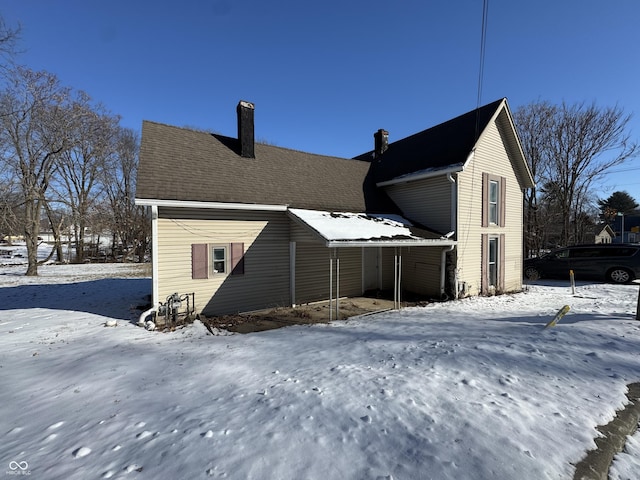 snow covered rear of property featuring a chimney