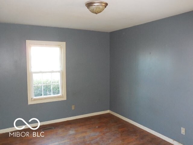 empty room with dark wood-type flooring, visible vents, and baseboards