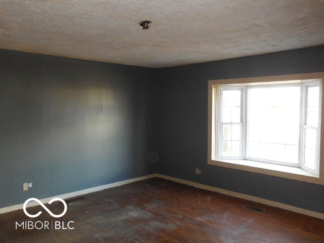 unfurnished room with baseboards, visible vents, a textured ceiling, and wood finished floors