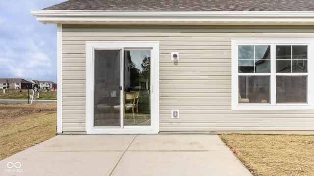 property entrance featuring a shingled roof and a patio