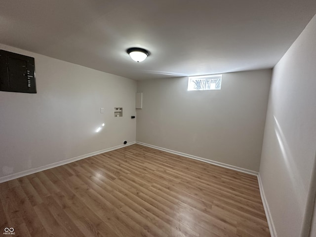 below grade area with light wood finished floors, electric panel, and baseboards