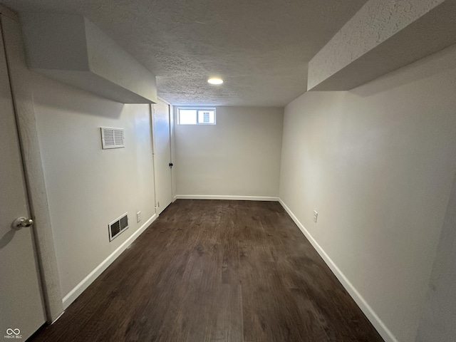 below grade area with a textured ceiling, dark wood-style floors, visible vents, and baseboards