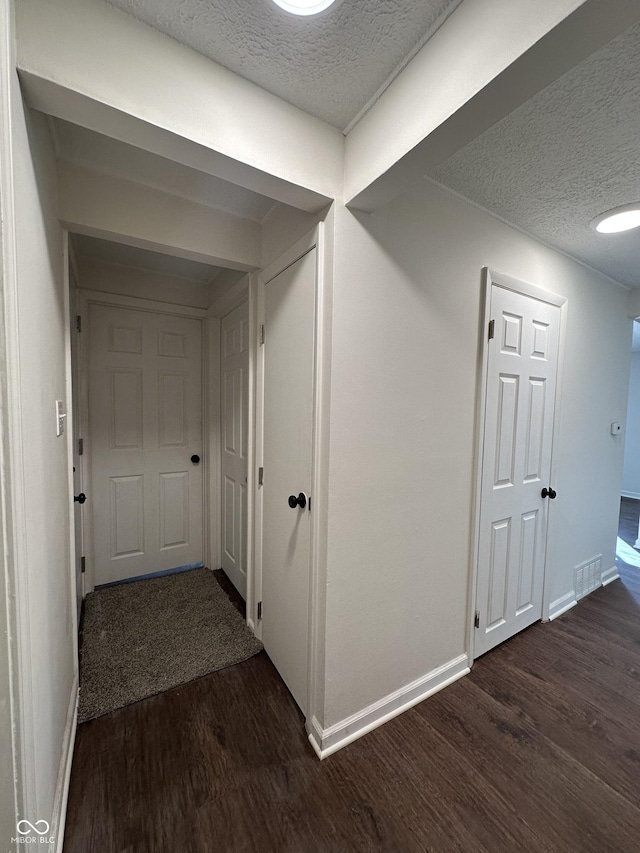 hallway with dark wood-type flooring, visible vents, a textured ceiling, and baseboards