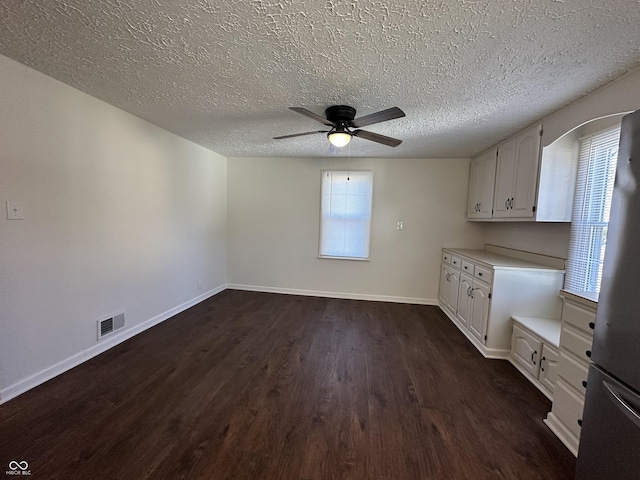 interior space with ceiling fan, a textured ceiling, dark wood-style flooring, visible vents, and baseboards