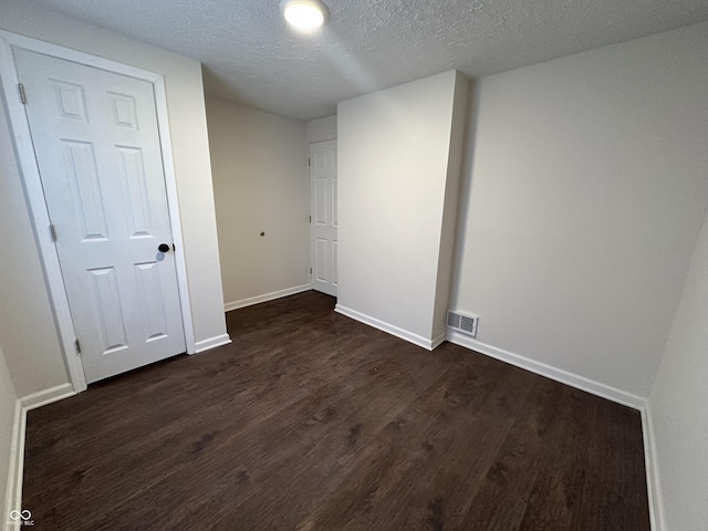 empty room with visible vents, baseboards, dark wood finished floors, and a textured ceiling