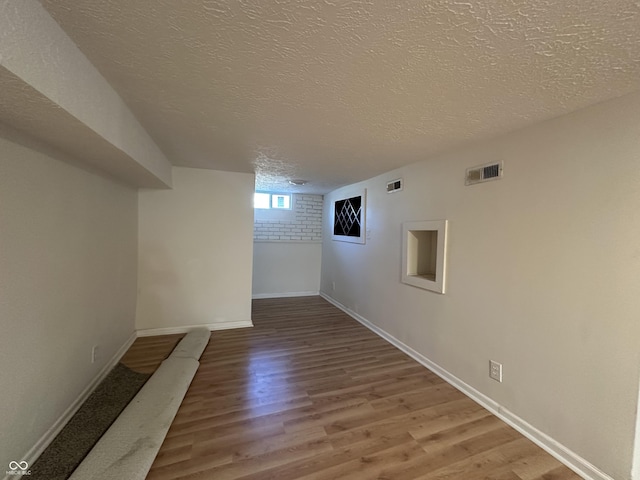 below grade area featuring baseboards, visible vents, light wood-style flooring, and a textured ceiling