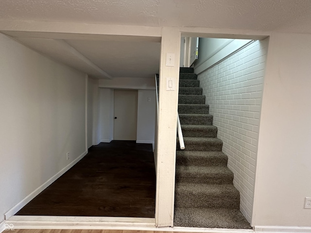 staircase featuring a textured ceiling, brick wall, wood finished floors, and baseboards