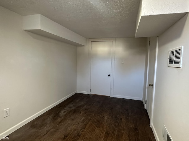 basement with dark wood-style floors, visible vents, a textured ceiling, and baseboards