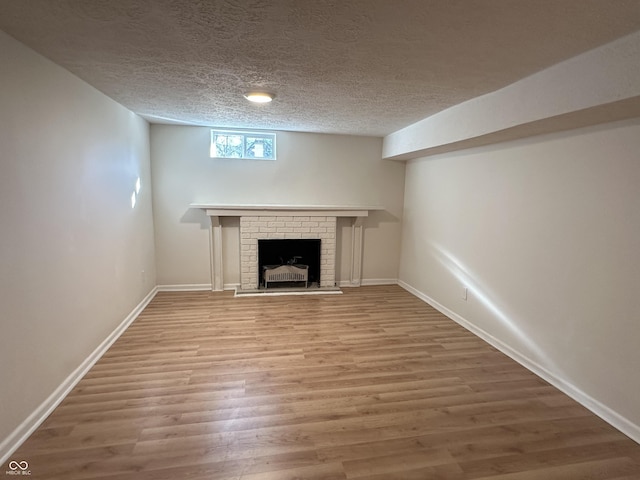 interior space with a brick fireplace, a textured ceiling, baseboards, and wood finished floors