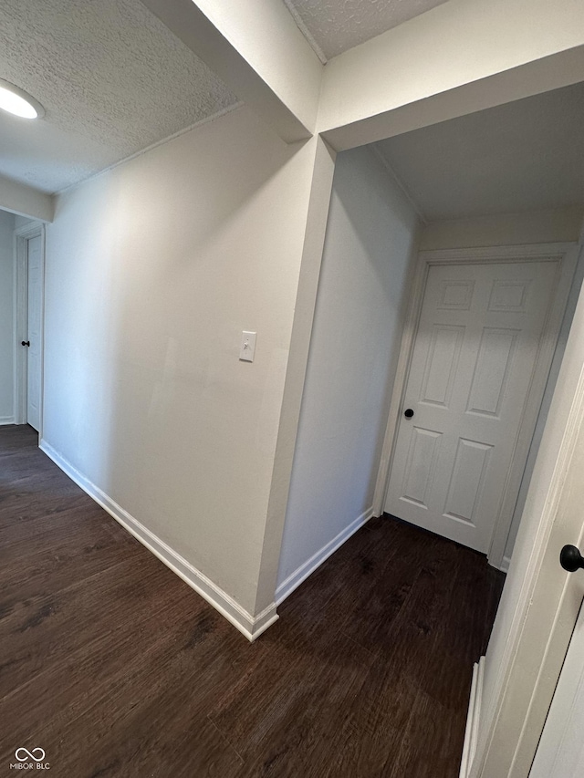 corridor with a textured ceiling, dark wood-style flooring, and baseboards