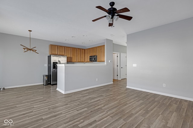 unfurnished living room with light wood-style flooring, baseboards, and ceiling fan with notable chandelier