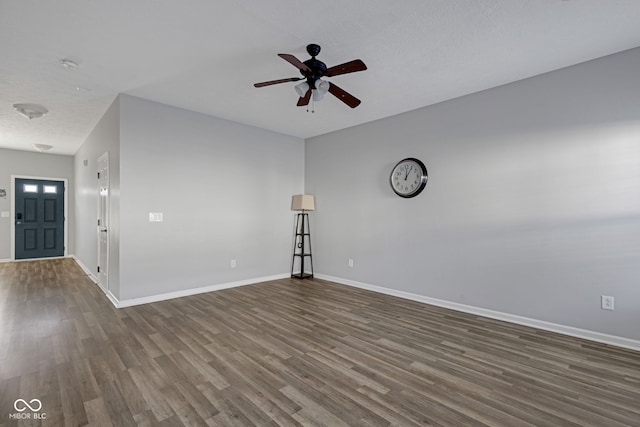 spare room featuring a ceiling fan, dark wood-style flooring, and baseboards