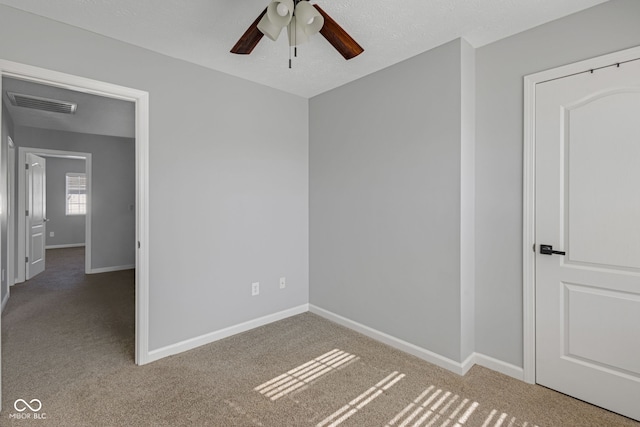 carpeted empty room with a ceiling fan, visible vents, a textured ceiling, and baseboards