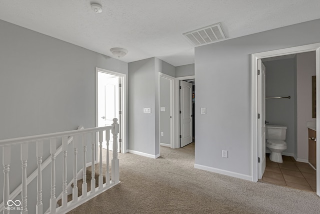 hallway with carpet flooring, visible vents, a textured ceiling, and an upstairs landing