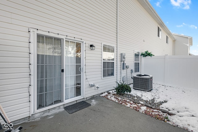 view of exterior entry with visible vents, fence, a patio, and central AC unit