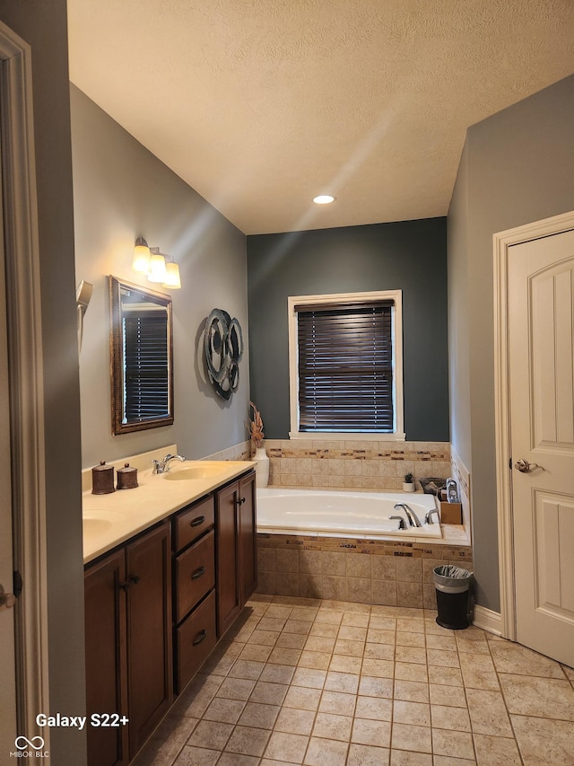 bathroom with double vanity, tile patterned floors, a garden tub, a textured ceiling, and a sink