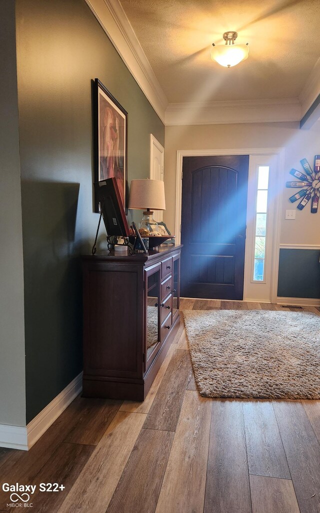 foyer entrance with ornamental molding, baseboards, a textured ceiling, and hardwood / wood-style floors