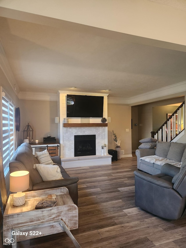 living room featuring dark wood-style flooring, crown molding, a fireplace with raised hearth, stairway, and baseboards