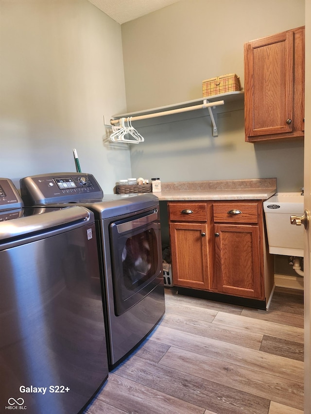 laundry area featuring light wood-type flooring, cabinet space, a sink, and washing machine and clothes dryer