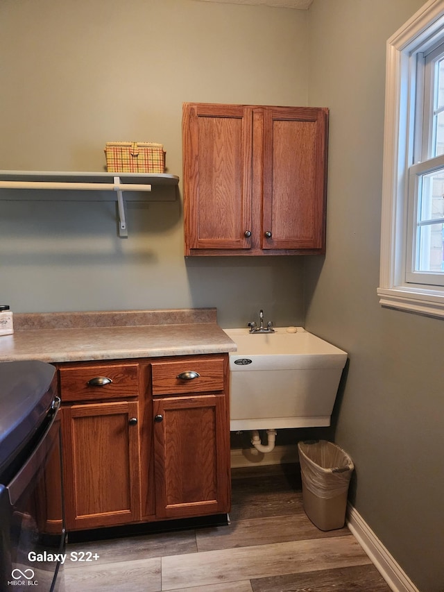 laundry area with cabinet space, a sink, light wood-style flooring, and baseboards