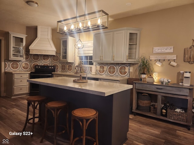 kitchen featuring dark wood-style floors, black range with electric stovetop, light countertops, premium range hood, and backsplash