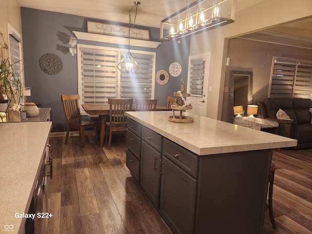 kitchen with a kitchen breakfast bar, dark wood-style flooring, a center island, decorative light fixtures, and light countertops