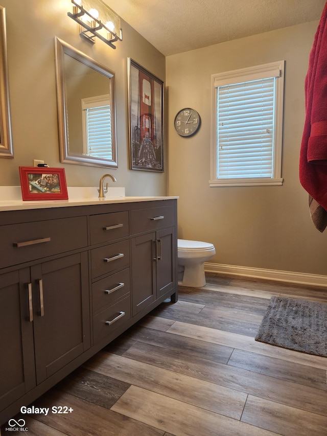 bathroom with a textured ceiling, toilet, wood finished floors, vanity, and baseboards