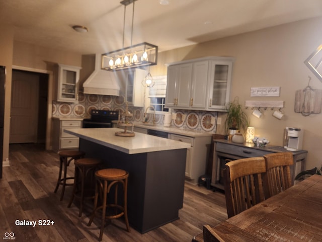 kitchen featuring light countertops, custom range hood, electric range, glass insert cabinets, and a kitchen breakfast bar