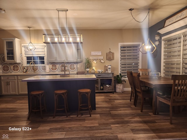 kitchen featuring a kitchen island, decorative backsplash, dark wood finished floors, and a sink