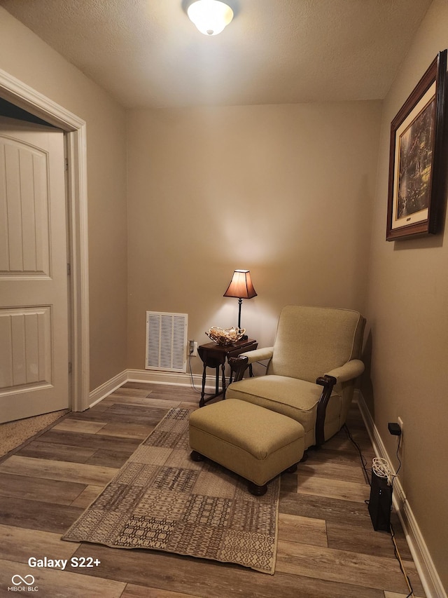 sitting room with visible vents, a textured ceiling, baseboards, and wood finished floors