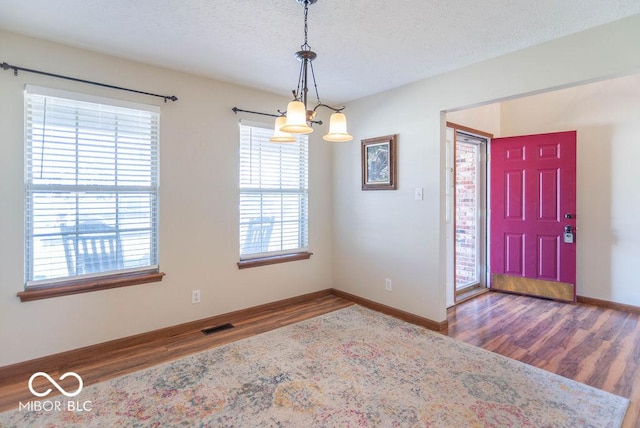 foyer featuring visible vents, baseboards, wood finished floors, a textured ceiling, and a chandelier