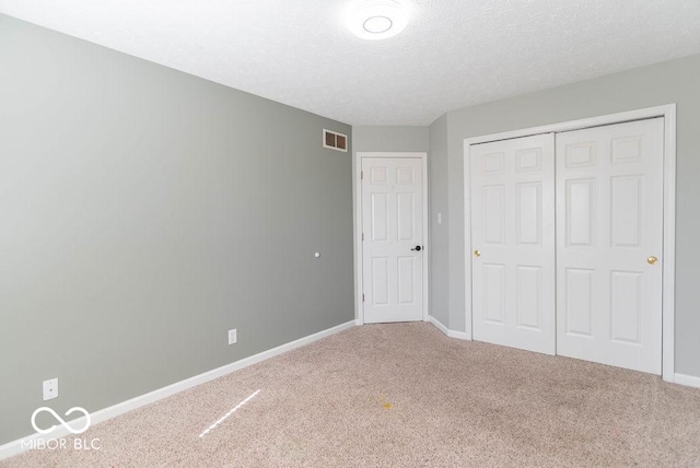 unfurnished bedroom featuring a textured ceiling, carpet flooring, visible vents, baseboards, and a closet