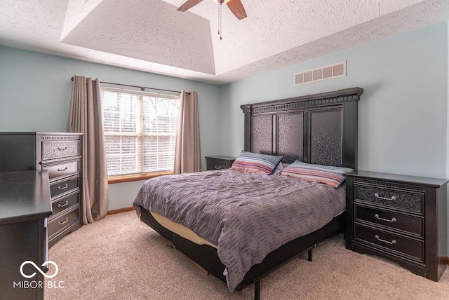 bedroom featuring a tray ceiling, visible vents, a ceiling fan, light carpet, and a textured ceiling