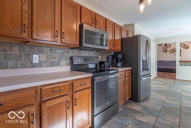 kitchen featuring brown cabinets, light countertops, decorative backsplash, appliances with stainless steel finishes, and a textured ceiling