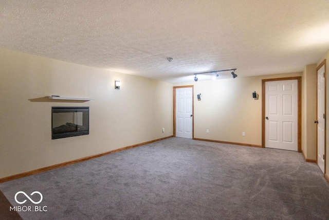 spare room featuring baseboards, a glass covered fireplace, carpet, a textured ceiling, and track lighting