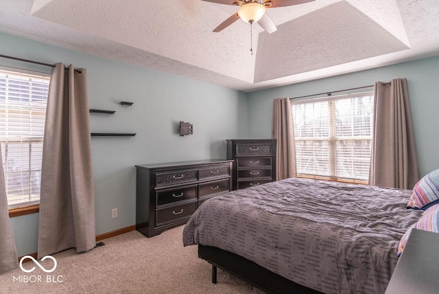 bedroom with a textured ceiling, ceiling fan, light colored carpet, baseboards, and a tray ceiling