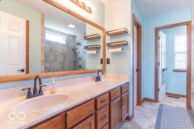 bathroom with a tile shower, double vanity, a sink, and baseboards