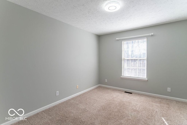 spare room featuring a textured ceiling, carpet floors, visible vents, and baseboards