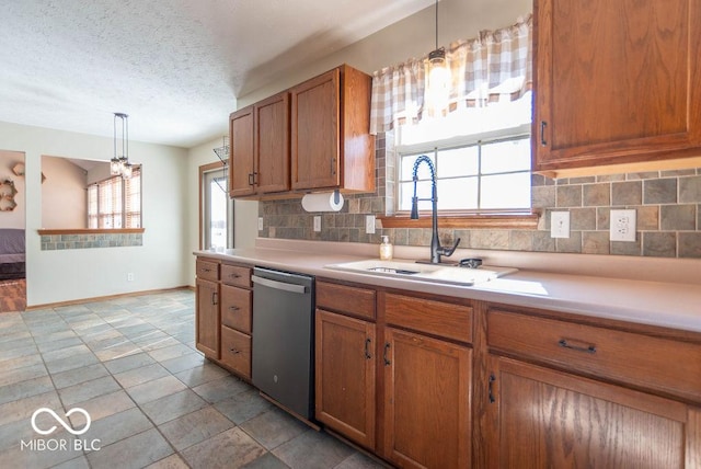 kitchen featuring a wealth of natural light, light countertops, stainless steel dishwasher, brown cabinetry, and a sink