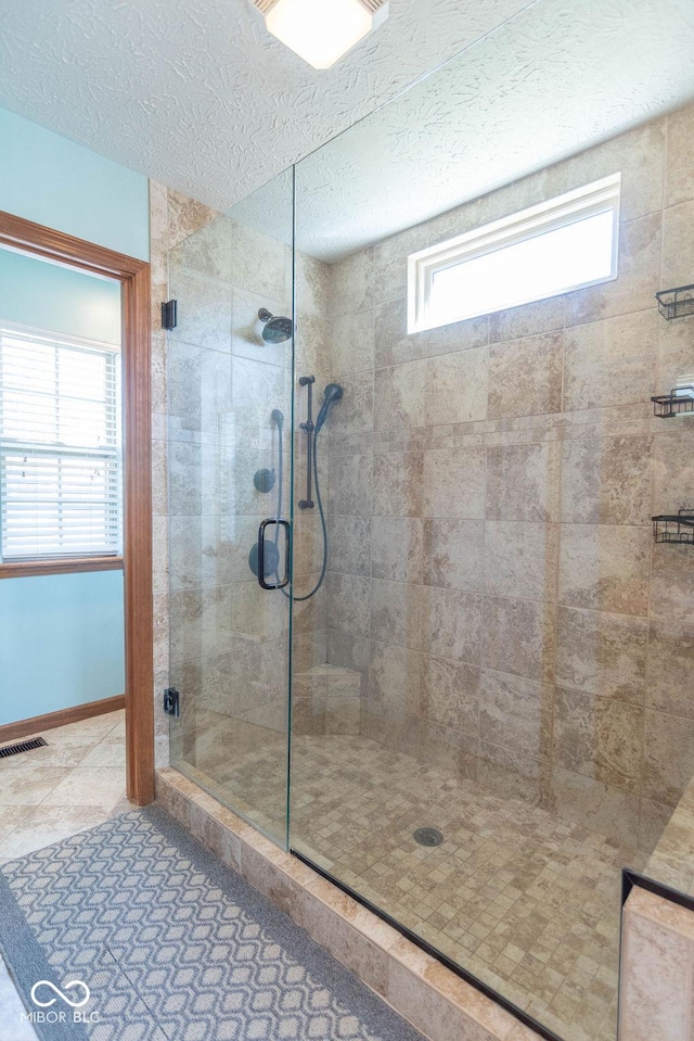 bathroom with a textured ceiling, a shower stall, visible vents, and baseboards