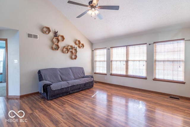 living room with a textured ceiling, vaulted ceiling, wood finished floors, and visible vents