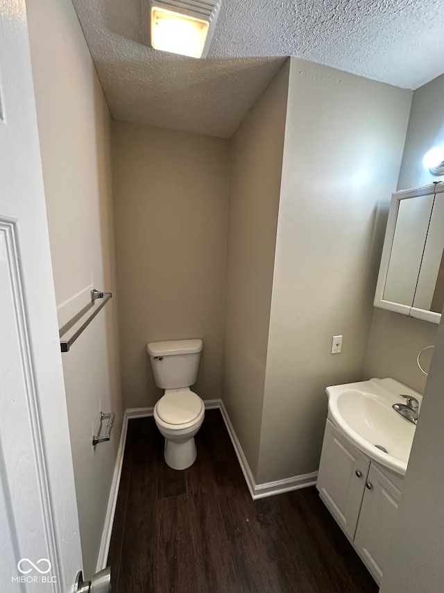 half bath featuring baseboards, a textured ceiling, wood finished floors, and vanity