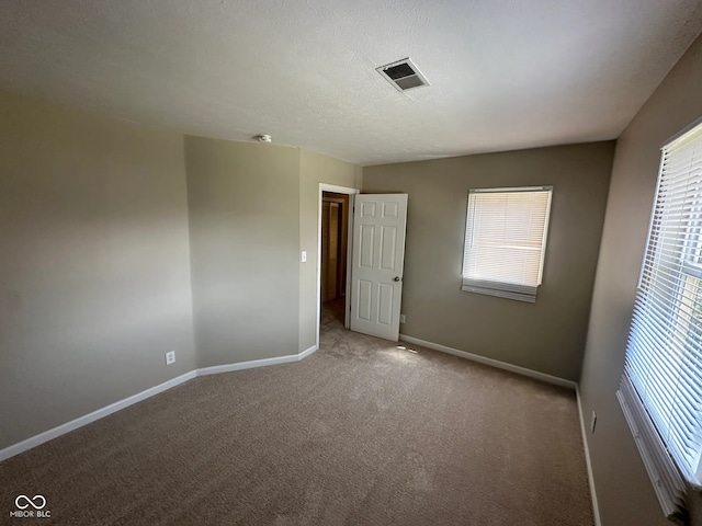 spare room featuring carpet floors, baseboards, visible vents, and a healthy amount of sunlight