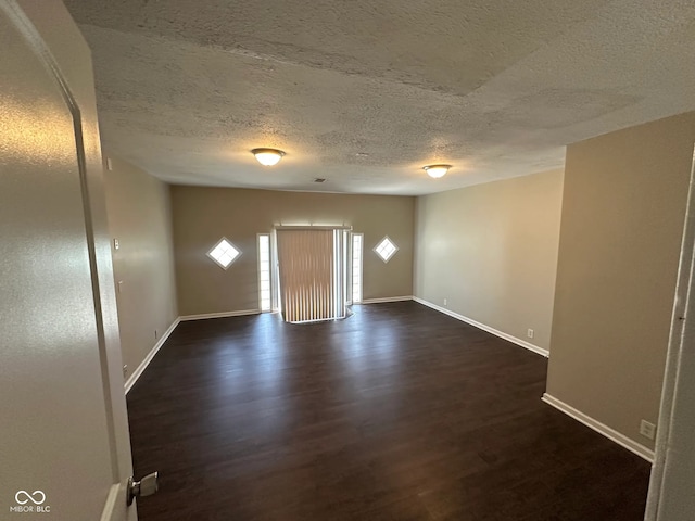 spare room featuring baseboards, dark wood finished floors, and a textured ceiling
